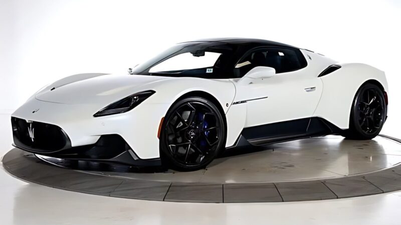 A white Maserati MC20 sports car with black accents is parked on a circular platform in a well-lit indoor setting—an exceptional choice for sale among the best supercars under $200k.