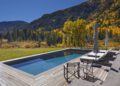 Rectangular outdoor pool with lounge chairs and umbrellas on a wooden deck, surrounded by grassy lawn and autumn Aspen trees, perfect for Outdoor Mountain Living with stunning mountain views in the background.