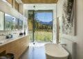 Modern Aspen bathroom with a freestanding tub, double sink, walk-in shower, large window, and scenic mountain view—perfect for embracing outdoor mountain living.