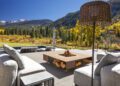 Outdoor patio with cushioned seating and a central fire pit, perfect for embracing Outdoor Mountain Living, overlooking a pool and Aspen’s forested mountains under a clear blue sky.