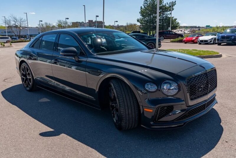 A black Bentley sedan, one of the best Bentleys, is parked in a sunlit lot with other cars and trees in the background.