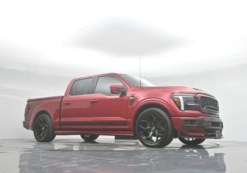 A red four-door Ford F-150 pickup truck with black wheels is parked in a plain, white, indoor studio setting. This stunning Shelby Trucks model is for sale.