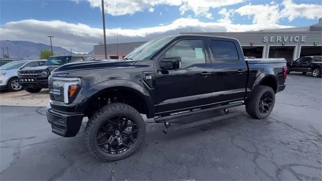 A black Ford F-150 with large black wheels and a crew cab is parked outside a service center on a paved lot under a partly cloudy sky, Shelby Trucks for sale.