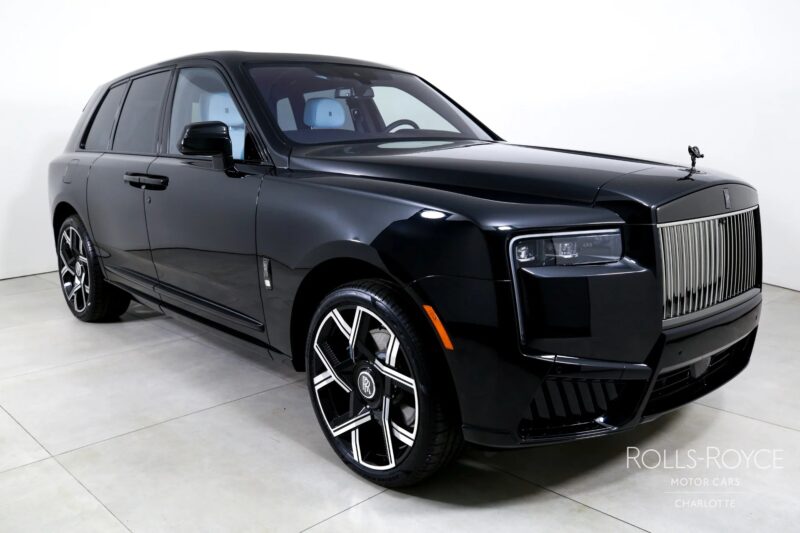 A black Rolls-Royce Cullinan luxury SUV is parked indoors on a light-colored floor with white walls in the background.