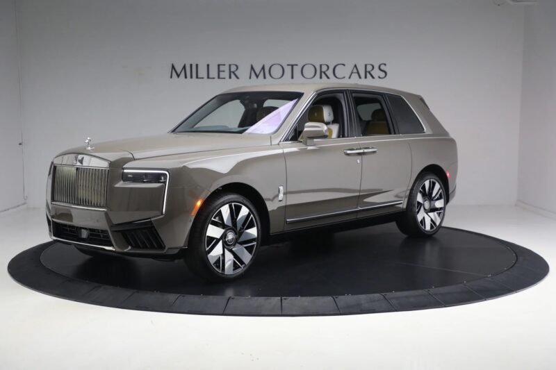 A metallic brown Rolls-Royce Cullinan luxury SUV is displayed in a showroom with "Miller Motorcars" on the wall behind it.