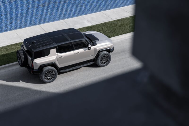 A silver GMC HUMMER EV electric vehicle is parked on a street next to a sidewalk and blue-tiled wall, viewed from above.