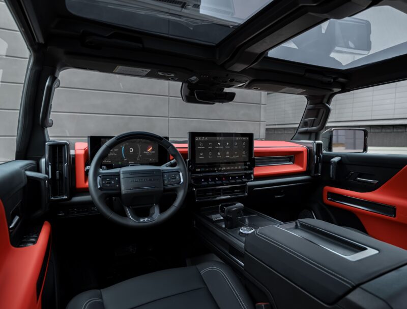 Interior view of the 2026 GMC HUMMER EV electric vehicle featuring a digital dashboard, large central touchscreen, orange accents, and a panoramic sunroof.