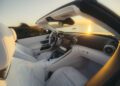 Interior of a modern white 2026 Mercedes-Maybach SL 680 convertible with leather seats and digital display, parked by the water at sunset.