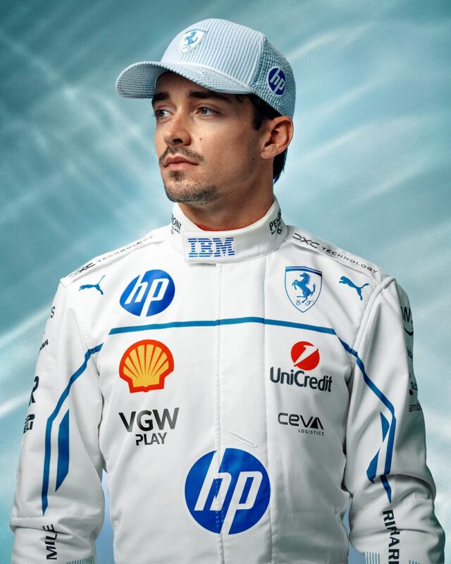 Charles Leclerc, wearing a white and blue Ferrari racing suit and a PUMA Hat, stands against a blue gradient background, looking slightly to the side. Sponsor logos are visible on the suit, evoking the spirit of the Monaco Grand Prix.