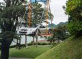A luxury Mercedes-Benz CLK GTR is being lifted by a crane on a large metal platform in a park-like area near a body of water and trees, making for an impressive scene ahead of FuoriConcorso 2025.