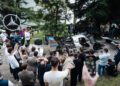 A crowd gathers around a Mercedes-Benz CLK GTR with its engine exposed at FuoriConcorso 2025, surrounded by trees and a large Mercedes-Benz logo.