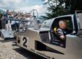 A man sits in a vintage race car marked with the number 2, surrounded by spectators taking photos at FuoriConcorso 2025 on a sunny day.