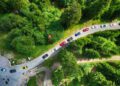 Aerial view of a line of colorful Ferraris driving along a winding road through a dense green forest, capturing the excitement of the Cavalcade Siviglia event in stunning Andalusia.