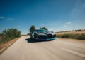 A Bugatti with blue accents speeds down a rural road in Portugal, surrounded by fields and a clear blue sky during the Grand Tour 2025.