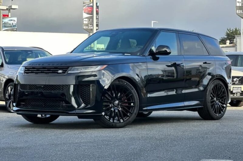 A black Range Rover SV Carmel Edition SUV is parked in a lot on a cloudy day, with other vehicles and Exclusive Rovers for Sale signs visible in the background.