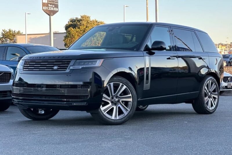 A black Range Rover SV Carmel Edition SUV is parked in a lot on a sunny day, with other vehicles and an Exclusive Rovers for sale dealership sign visible in the background.