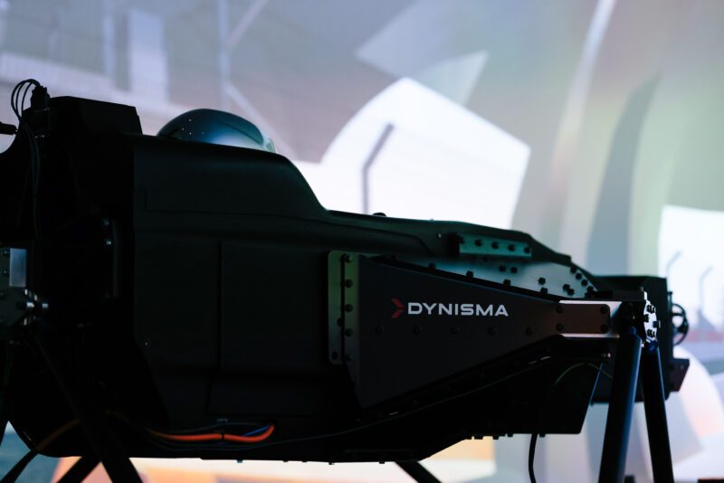 Close-up of a DYNISMA GMR-001 Hypercar Simulator cockpit in a dark room, with abstract light patterns in the background, creating an immersive virtual racing atmosphere.