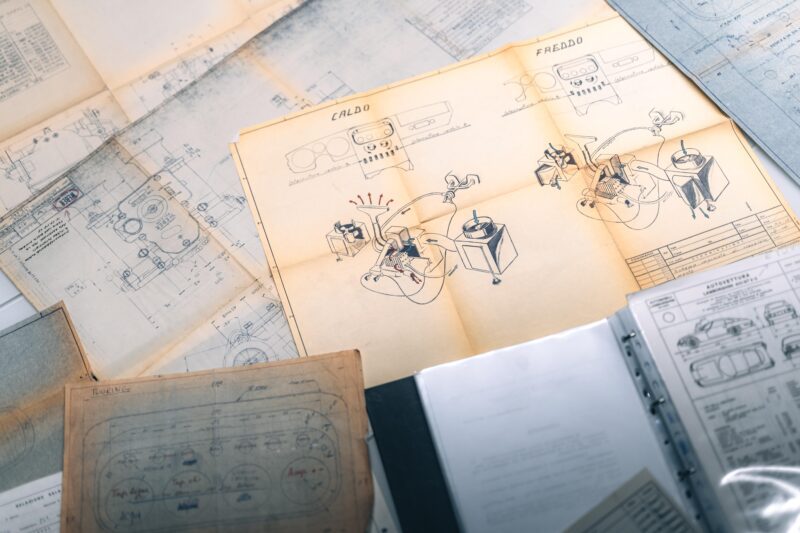 A collection of technical drawings and blueprints on a table, including illustrated instructions labeled "CALDO" and "FREDDO" in Italian, showcases Lamborghini’s rich automotive history and the archival work of Polo Storico.