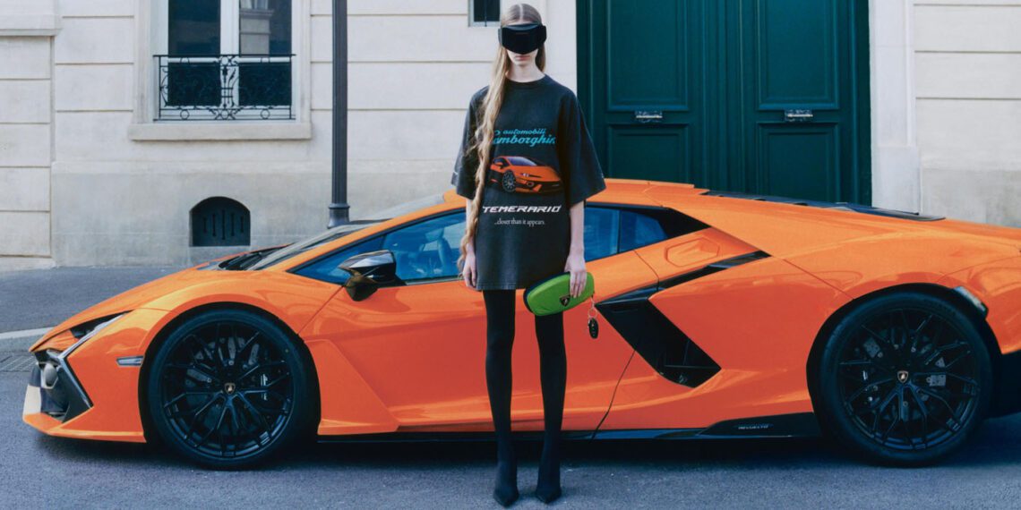 A person wearing black Balenciaga clothing, a visor, and holding a green clutch stands in front of an orange Lamborghini parked on a city street.