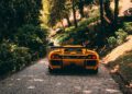 A yellow Lamborghini sports car, a true classic among race cars, is parked on a gravel path surrounded by greenery and trees on a sunny day.