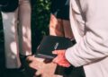 A person in a white jacket holds a black folder while standing next to two others outdoors at Villa d'Este during FuoriConcorso.