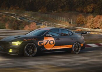 A black Genesis sports sedan with orange "G70" and "Nordschleife" decals races on a curvy track, embraced by autumn trees and metal guardrails—capturing the spirit of a G70 Track Day Special Concept.