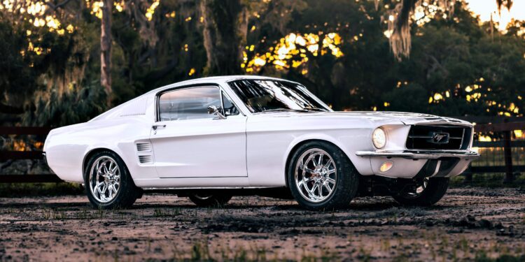 A classic white Ghost Mustang Fastback parked outdoors on a dirt surface, with trees and a wooden fence in the background—a nod to modern muscle and Roush Performance heritage.