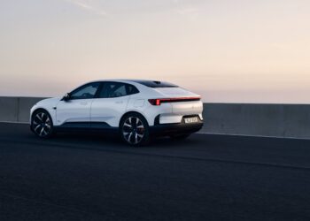 A white electric car drives on an empty road next to a concrete barrier at sunset.