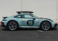 A light blue Porsche 911 Dakar with black racing decals, number 19 on the door, roof rack, and Shell and Bosch sponsor logos, is parked by a plain wall—truly one of the best Porsche 911 models for adventure seekers.