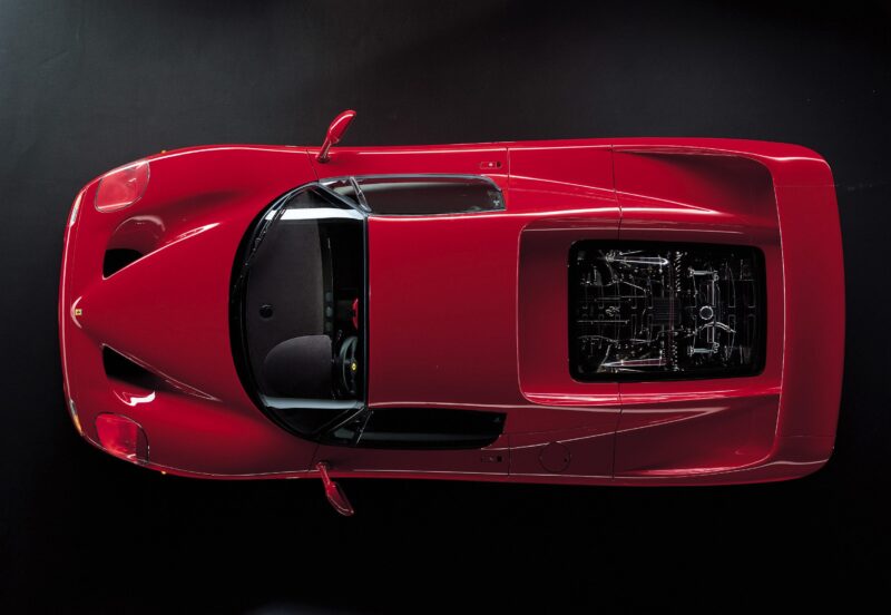 Top-down view of a Ferrari F50 with a visible engine compartment, black windshield, and sleek aerodynamic design on a dark background—celebrating the 30th Anniversary Legacy Tour.