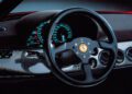 Close-up of a Ferrari F50 steering wheel and dashboard, featuring analog gauges, climate control vents, and a textured carbon fiber finish—celebrating the 30th Anniversary Legacy Tour.