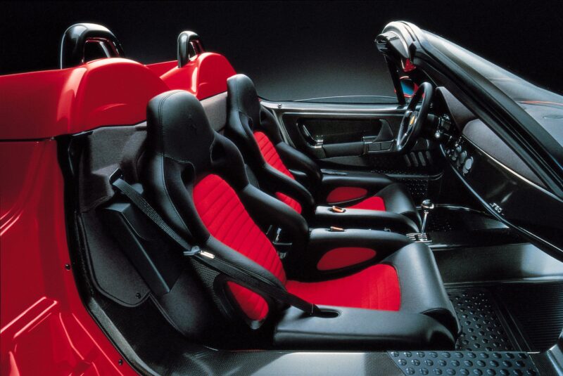 Interior of a Ferrari F50 with black and red bucket seats, exposed metal floor, and minimalist dashboard, photographed from the passenger side—a striking tribute to the Legacy Tour 30th Anniversary.