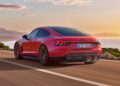 A red Audi e-tron GT makes its stunning debut, driving along a coastal road at sunset with mountains and water in the background.