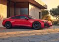 An affordable Audi e-tron GT sports sedan is parked on a stone driveway beside a modern house, with trees and sunset in the background.
