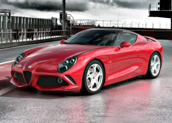 A shiny red sports car, the 1-of-1 Alfa Romeo DoppiaCoda by Zagato, is parked on a racetrack with a modern building and cloudy sky, highlighting the significance of this exclusive masterpiece.