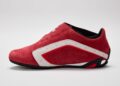 A red suede driving shoe with F1 DNA, featuring a white stripe and black details, viewed from the side against a plain light background.