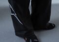 Person wearing black pants with a white graphic design and black socks with white and red symbols, standing on a gray floor and rocking STARLINE Sneaker inspired by F1 DNA.