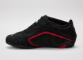 A black suede STARLINE Sneaker with red accents, low profile design, and a thin sole—showcasing F1 DNA—is presented in a side view against a plain light gray background.