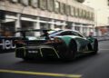 A green Aston Martin Valhalla speeds down a city racetrack, captured from the rear on a bright day, evoking the thrill of the Monaco Grand Prix.