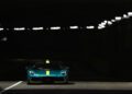 A green Aston Martin with a yellow racing stripe is illuminated under bright lights in an otherwise dark tunnel, evoking the thrill of the Monaco Grand Prix.