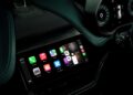 A car dashboard display screen shows various app icons and controls, with the volume adjustment overlay visible—much like when Aston Martin becomes the first automaker to debut Apple CarPlay Ultra.