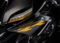 Close-up of a black Carbon-Clad Concept BMW Motorrad, with carbon fiber finish and yellow accents, showcasing the BMW logo and next-generation RR aerodynamic design elements.