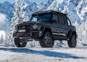 A black BRABUS XLP 800 ADVENTURE pickup truck, based on the Mercedes-AMG G63, is parked on a snowy mountain road with snow-covered trees and mountains in the background.