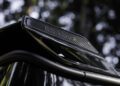 Close-up of a BRABUS logo on a carbon fiber car part, with blurred green foliage in the background—highlighting the signature style found on models like the G 63 and XL 800 Off-Roader.