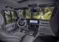 View of a modern BRABUS G 63 SUV interior with leather seats, digital displays, and forest scenery visible through the windshield and windows.