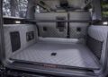 A view of a luxury SUV's cargo area in the BRABUS G 63 shows quilted grey leather upholstery, storage nets, a speaker, and a cargo bar, with rear seats folded forward.