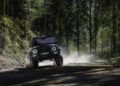 A BRABUS G 63 SUV drives on a dirt road through a dense forest, kicking up dust as it moves forward.