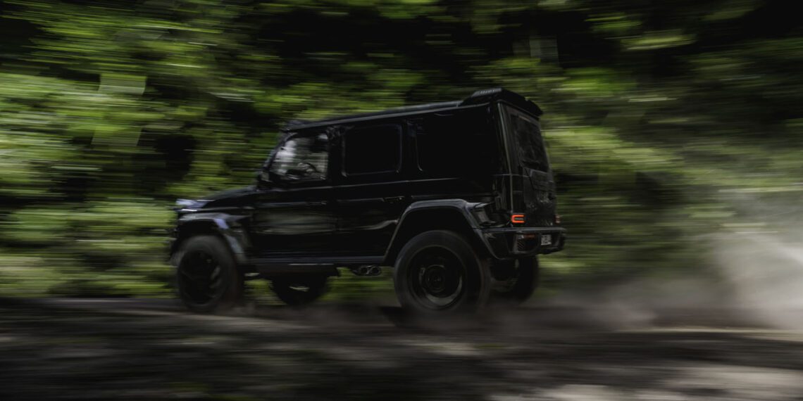 A BRABUS G 63 XL 800 Off-Roader speeds along a dirt road through a lush, green forest, with motion blur emphasizing the SUV’s power and agility.