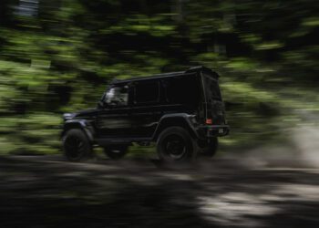 A BRABUS G 63 XL 800 Off-Roader speeds along a dirt road through a lush, green forest, with motion blur emphasizing the SUV’s power and agility.