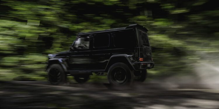 A BRABUS G 63 XL 800 Off-Roader speeds along a dirt road through a lush, green forest, with motion blur emphasizing the SUV’s power and agility.